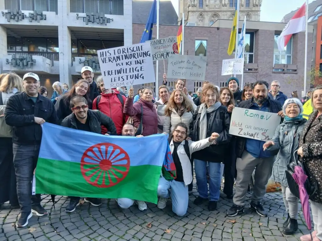 Mitglieder und Unterstützer:innen des Rom e.V. mit Roma-Flagge und Protestschildern bei der Kundgebung gegen die Kürzungen vor dem Kölner Rathaus